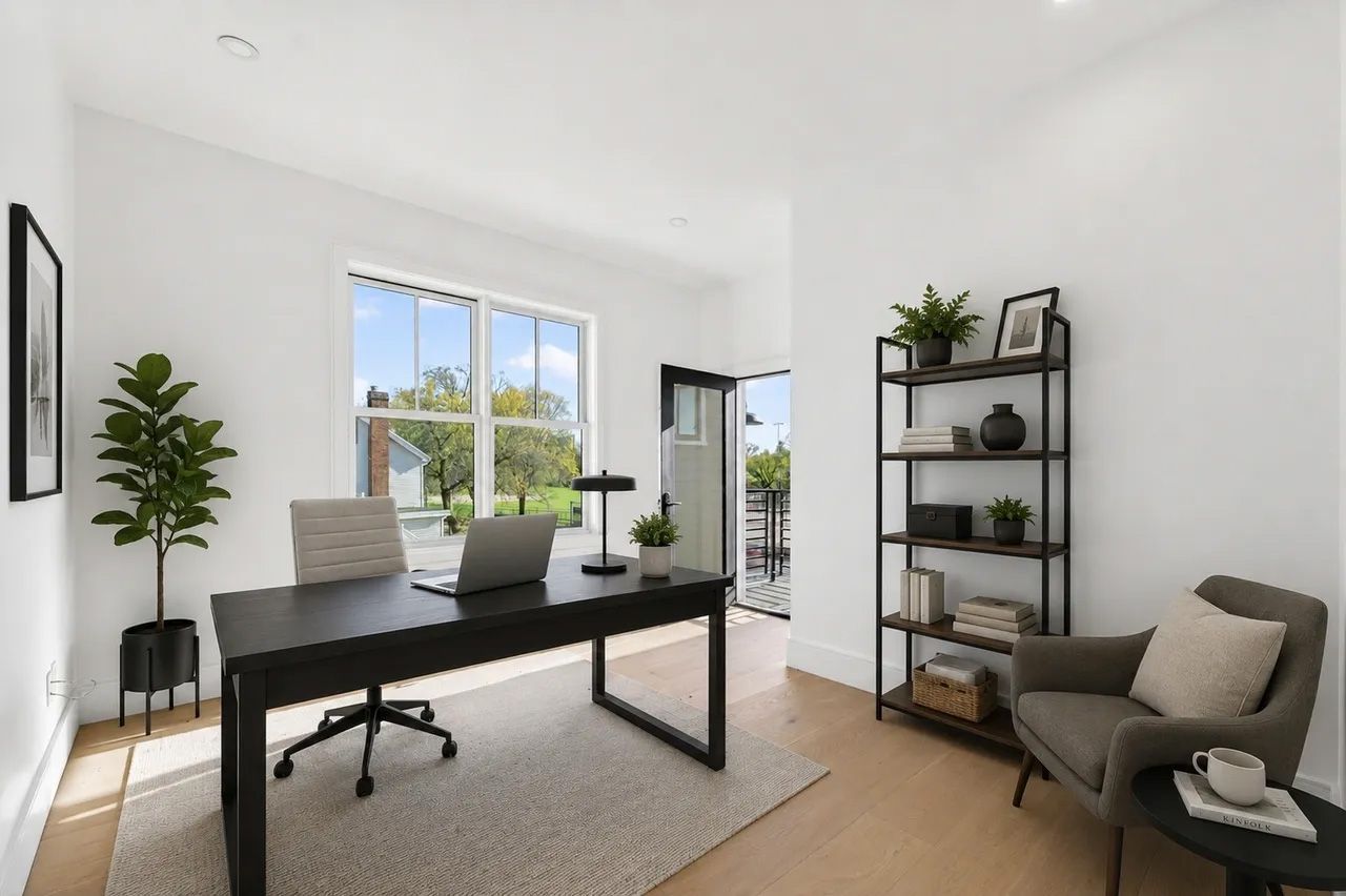 Bright modern home office with a black desk, laptop, chair, shelves, and a window with a potted plant.