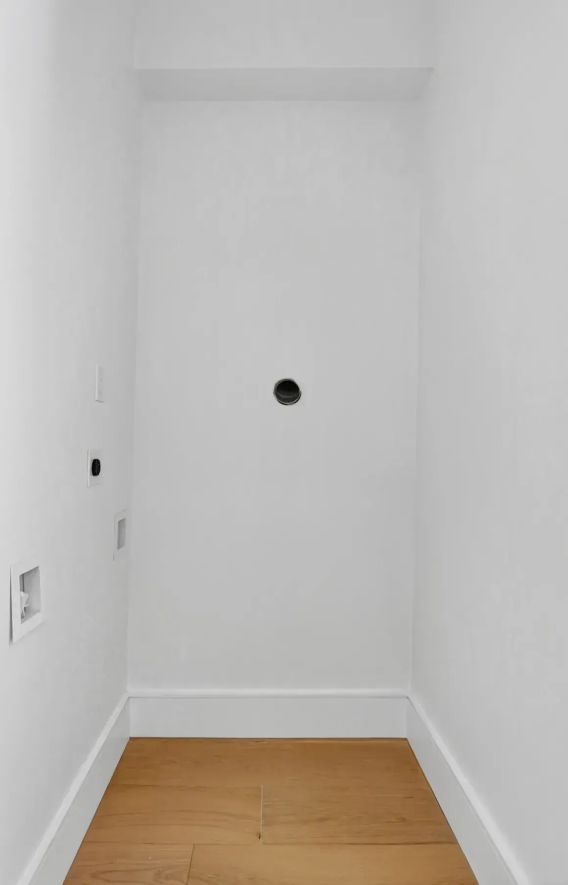 Narrow white alcove with a small black wall opening above a light wood floor