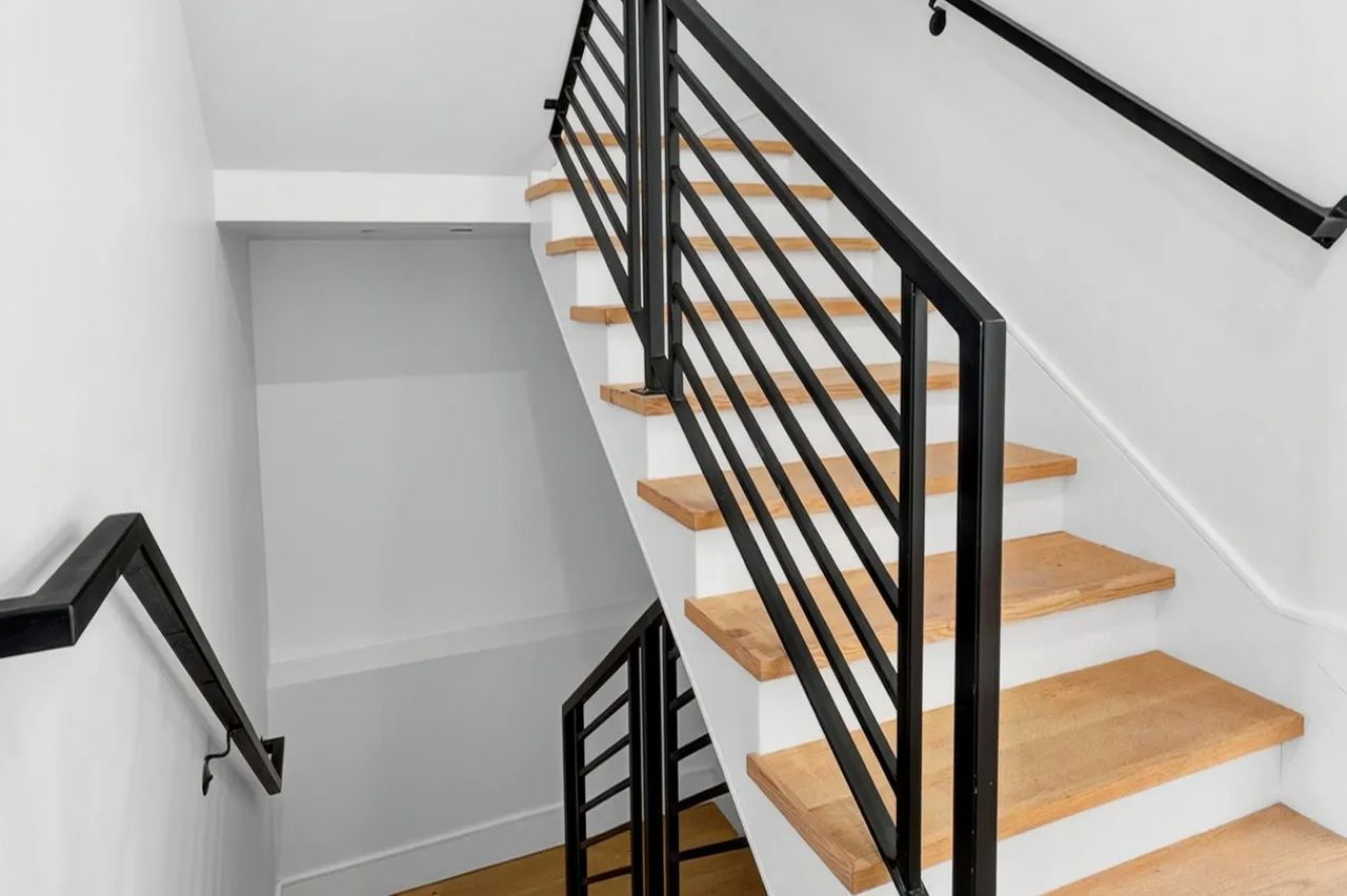 Stairwell with light wood steps, black metal railings, and white walls
