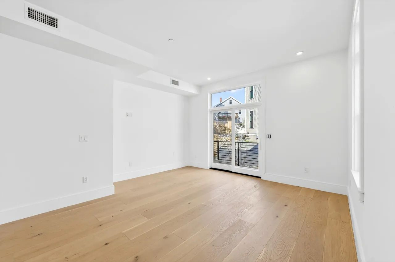Empty white room with light wood floors and French doors opening to a balcony.