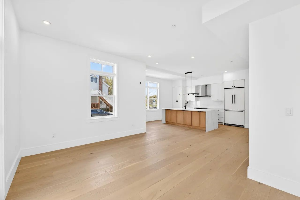Bright white open-plan kitchen and living space with light wood floors and island breakfast bar.