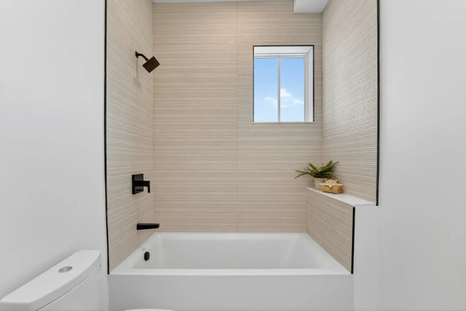 Modern bathroom with a bathtub, beige tile walls, black fixtures, and a small window