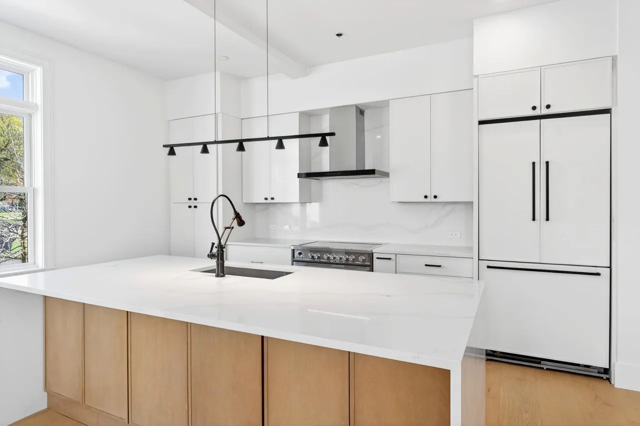 A bright white modern kitchen with island, black faucet, wood cabinets, and stainless steel appliances