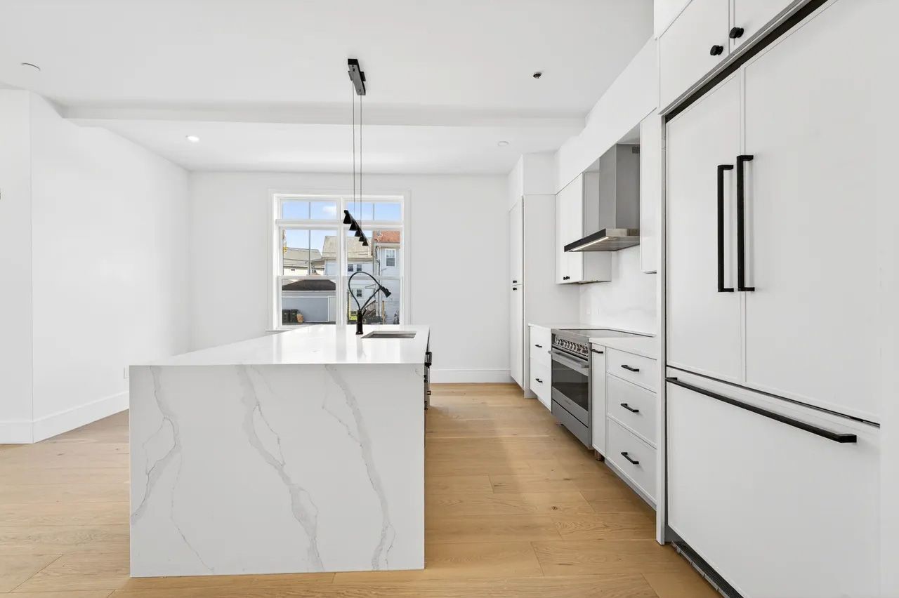 Bright modern kitchen with white cabinets, marble island, wood floor, and stainless steel appliances