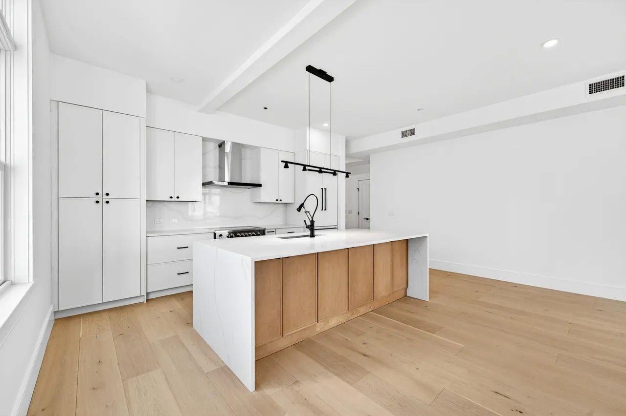 A bright modern white kitchen with wood island and hardwood floors in an open, empty room