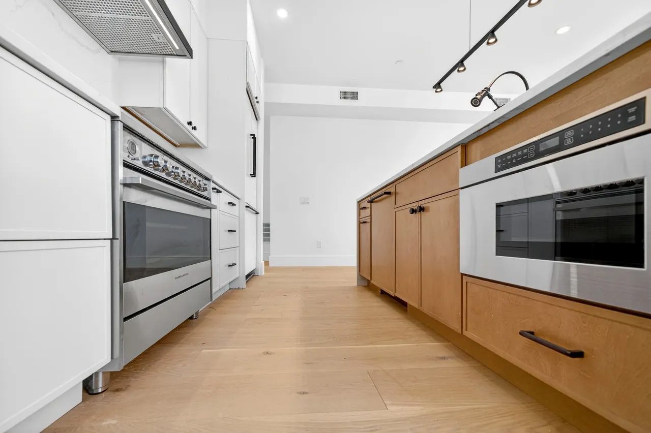 Modern kitchen with white and wood cabinets, stainless steel appliances, and light wood flooring