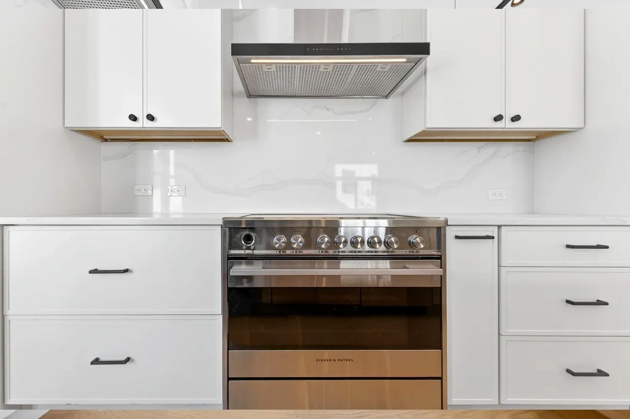 White kitchen with stainless steel oven, range hood, and built-in white cabinets