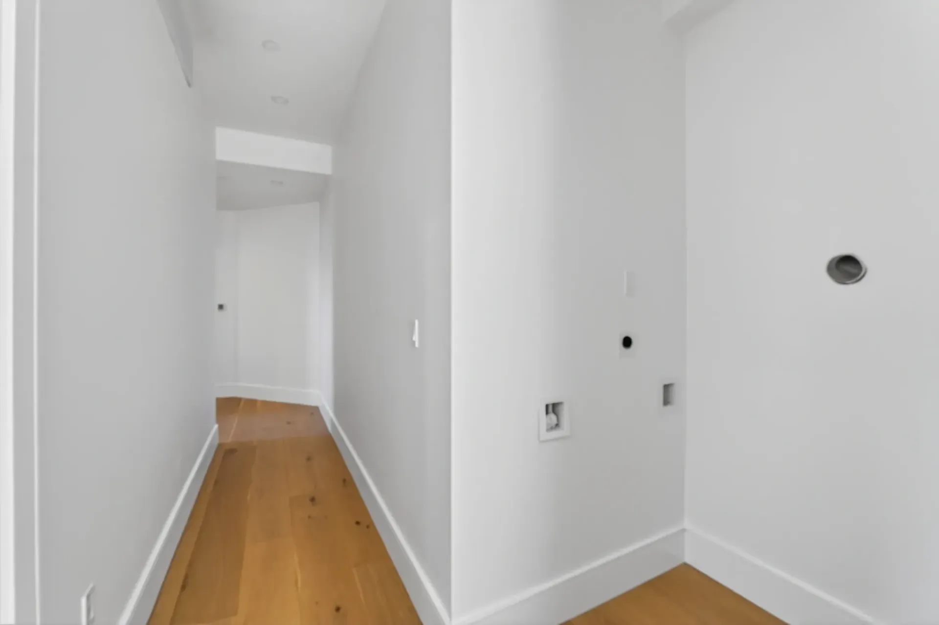 Empty white hallway with wooden floors and doorways leading to another room