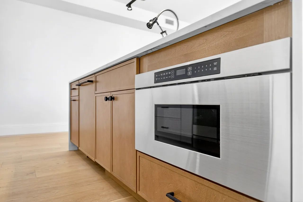Modern kitchen with wood cabinets and a stainless steel wall oven on a light wood floor