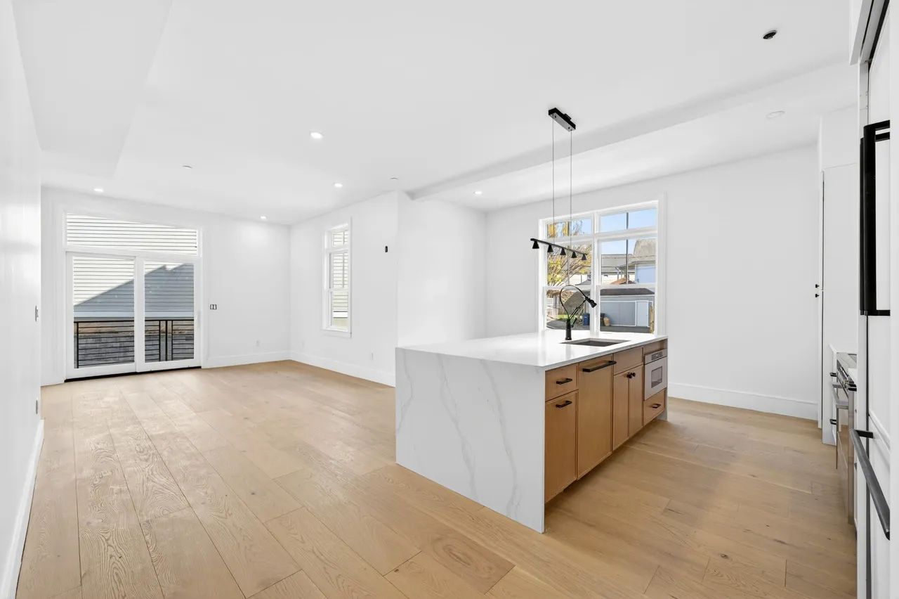Bright modern open-plan kitchen and living area with white walls, wood floors, and a central island.