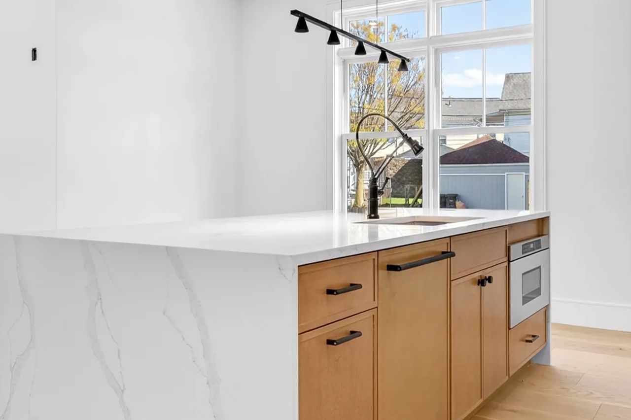 Modern kitchen island with white marble-look counter, wood drawers, black track lighting, and a window view