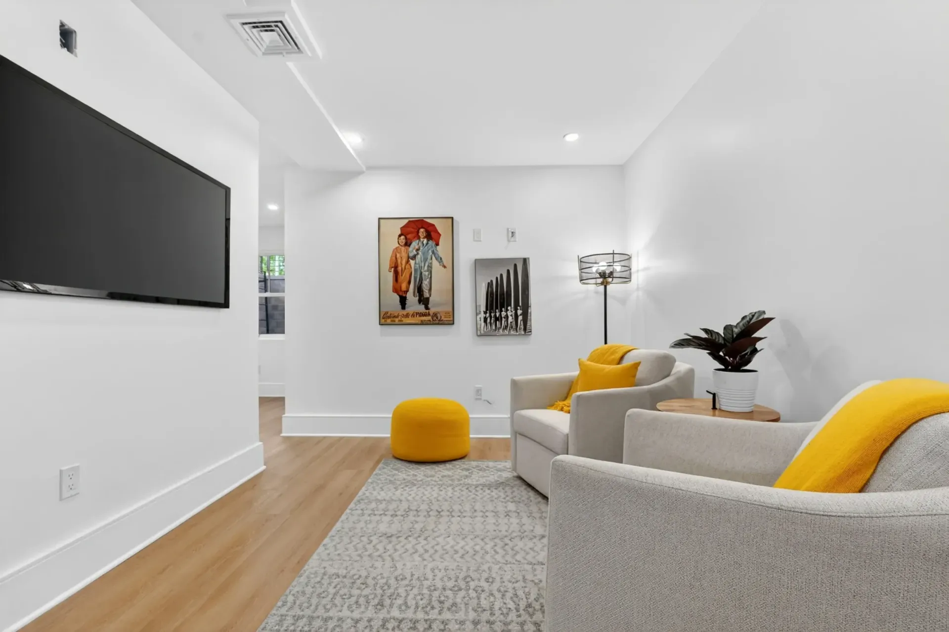 Modern living room with gray sofas, yellow accents, wall art, and a TV on a white wall.