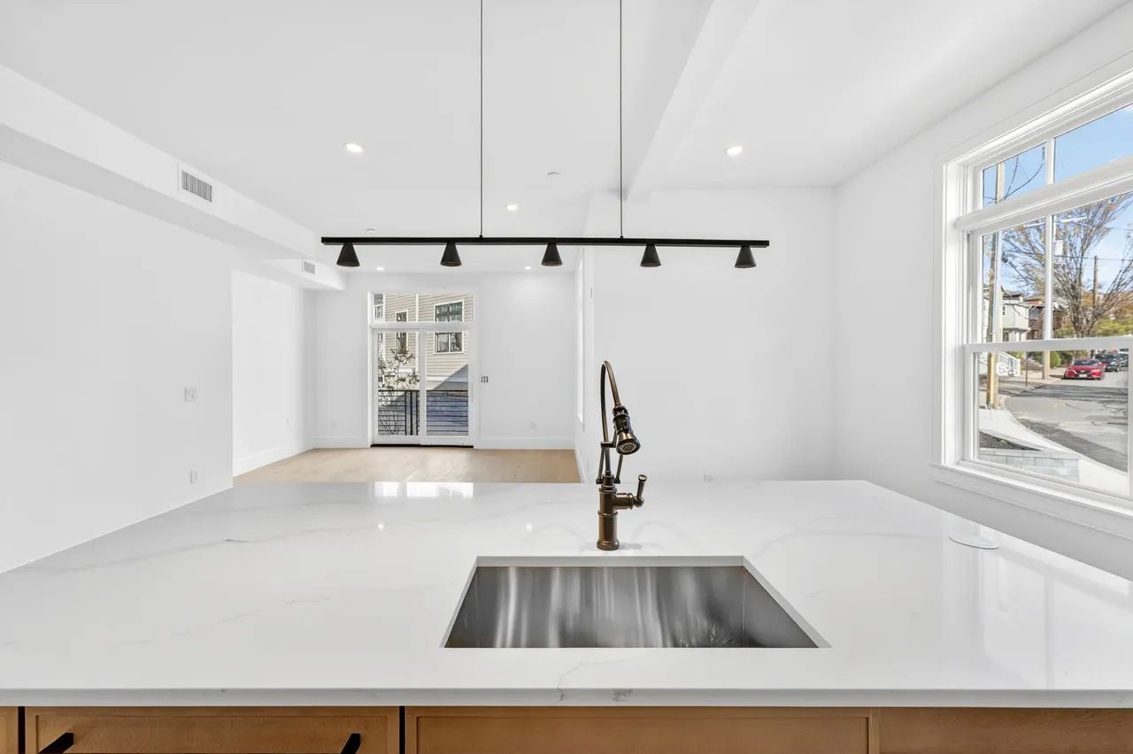 A bright white modern kitchen with island sink, black pendant lights, and large windows