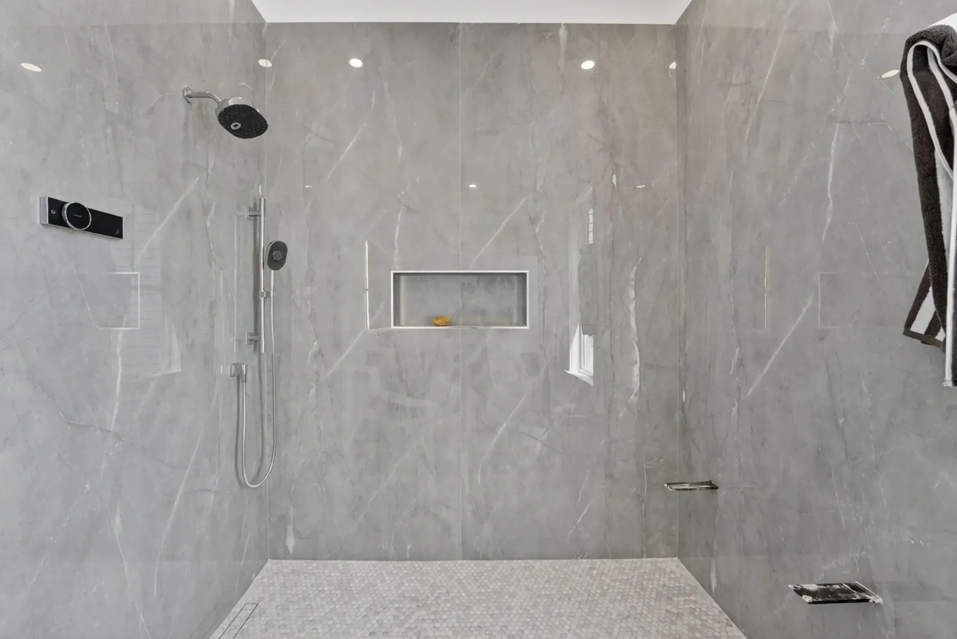 Gray tiled shower with a rainfall head, handheld sprayer, built-in niche, and bench.