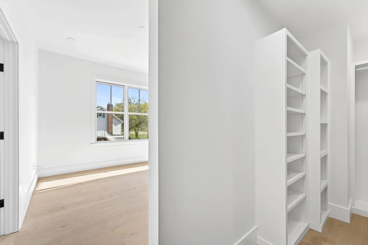 A bright white empty room with wood floors, a window seat, and built-in shelves.