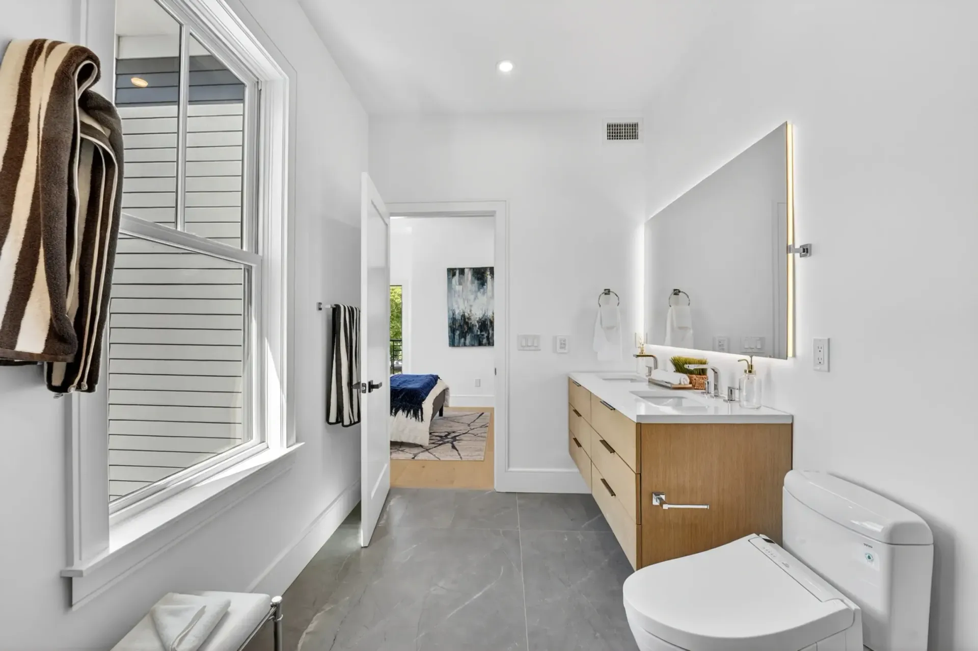 Modern white bathroom with double vanity, large mirror, shower, and gray tile floor.