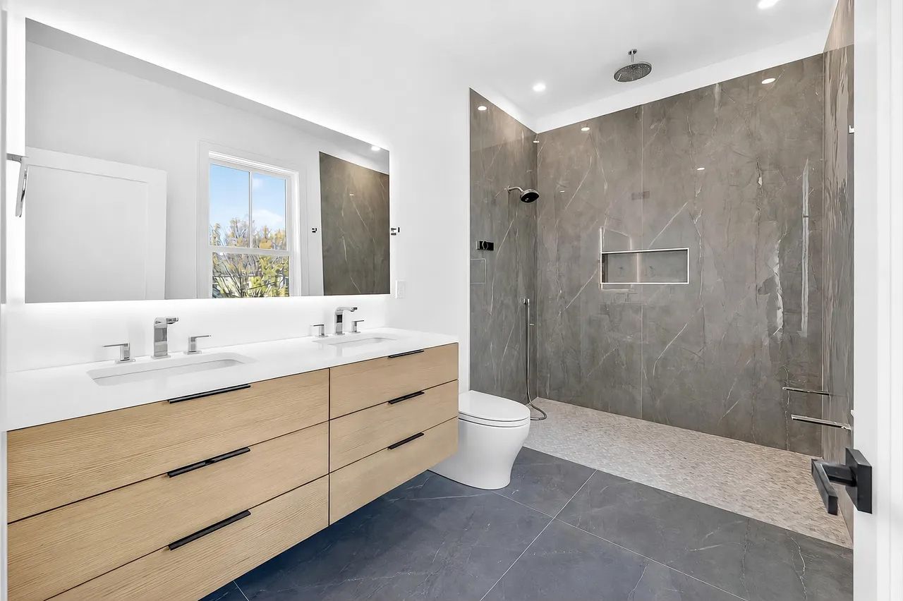 Modern bathroom with double vanity, large mirror, and gray tiled walk-in shower