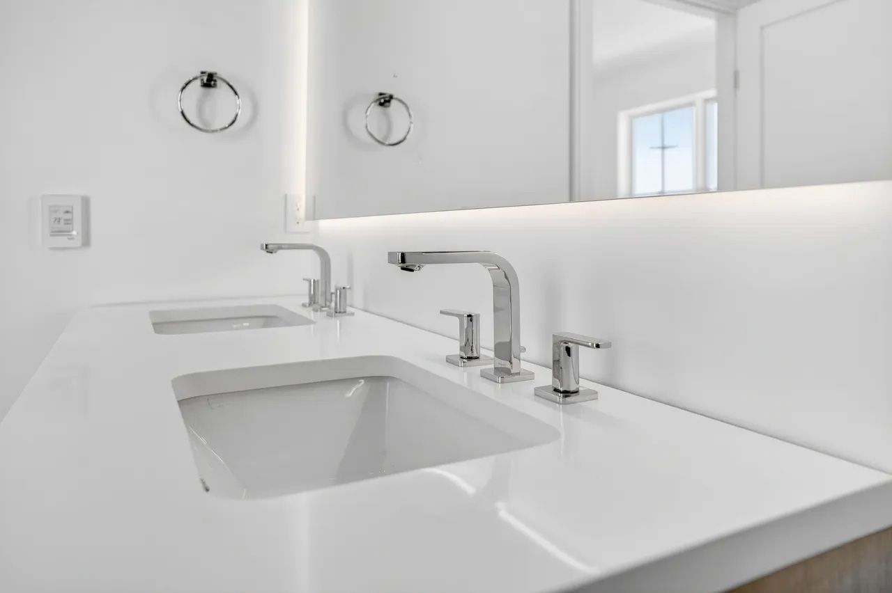 Minimalist white bathroom sink with chrome faucets and a large mirror above it