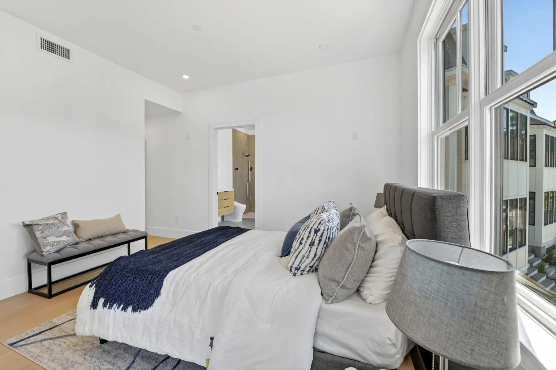 Bright white bedroom with a bed, bench, and large windows letting in natural light