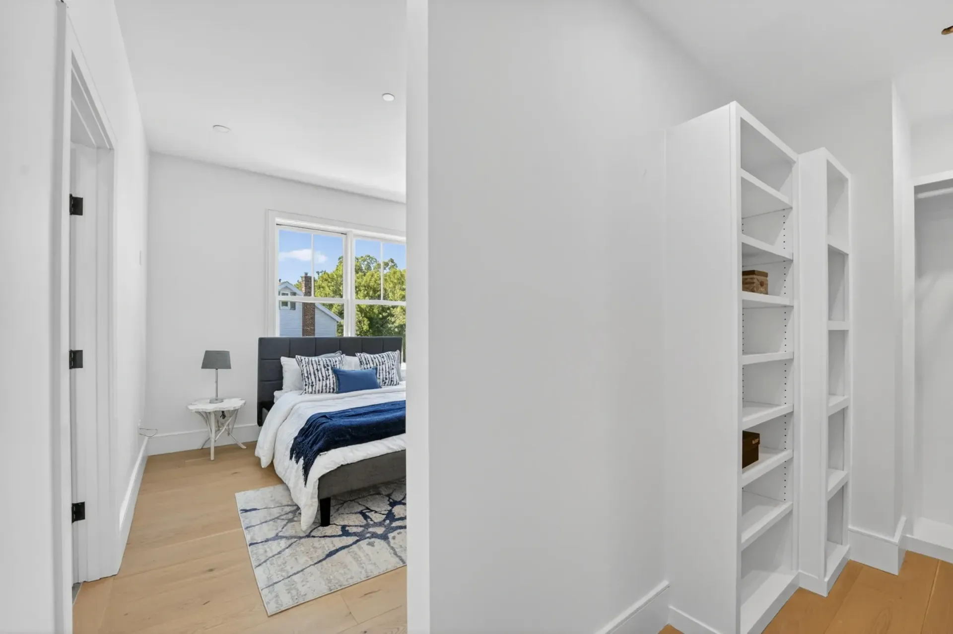 Bright white bedroom with navy bedding, window light, and a hallway view of built-in shelves