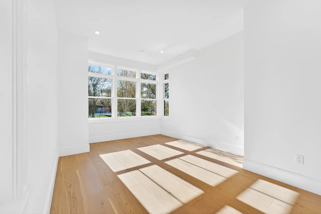 Bright empty room with white walls, wood floors, and sunlight streaming through large windows.