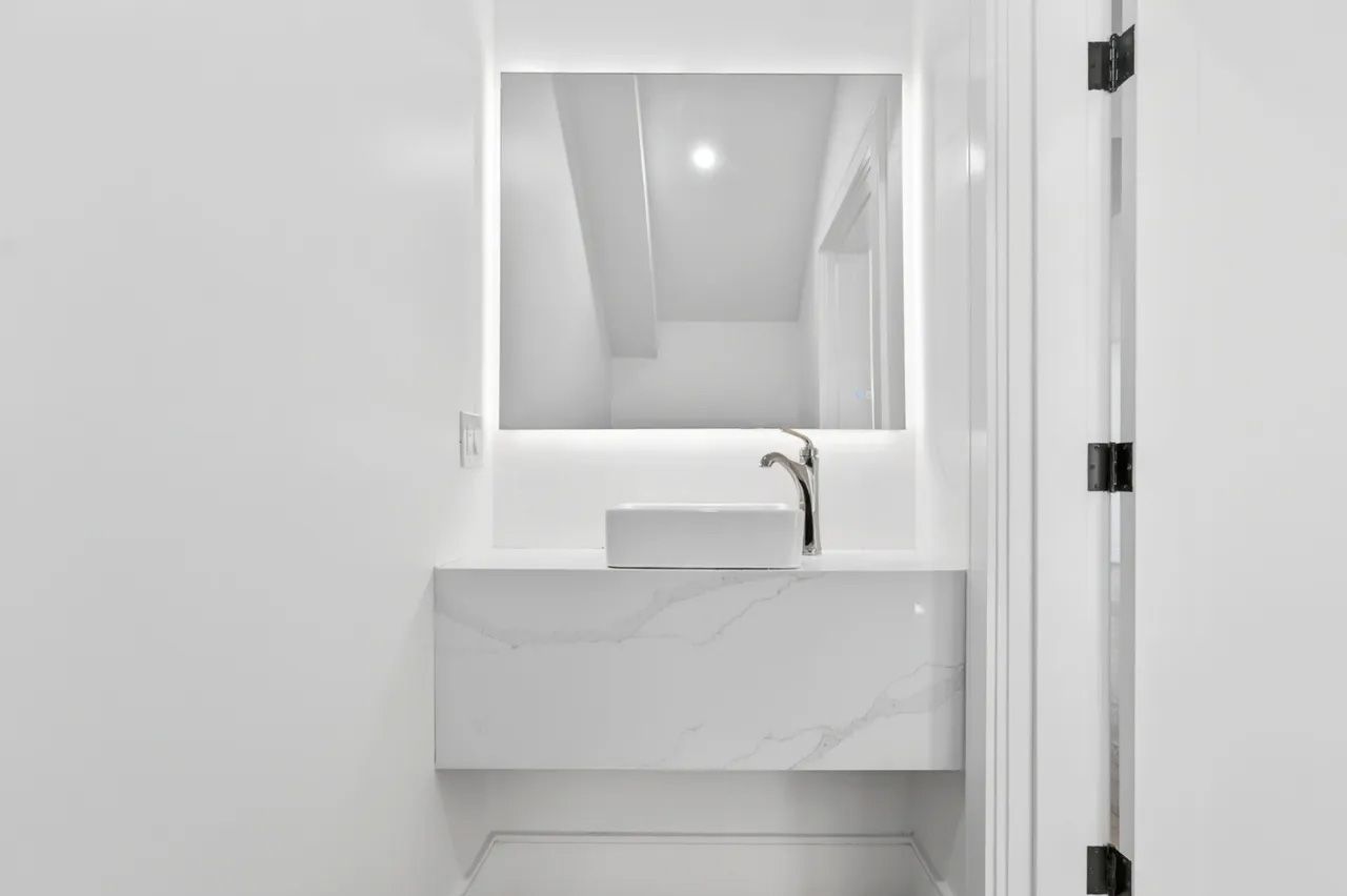 Minimal white bathroom vanity with mirror and chrome faucet in a bright, narrow space