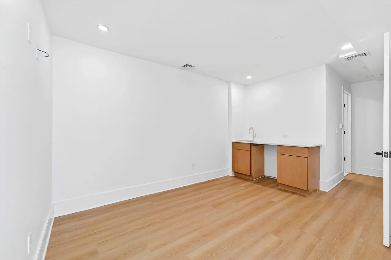 Empty modern kitchen with white walls, wood flooring, and a small sink cabinet along one wall