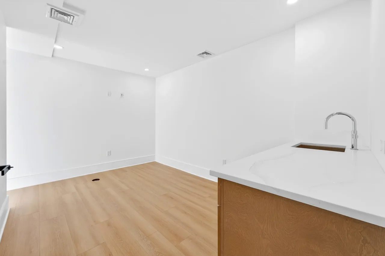 Empty white room with light wood floors and a small kitchen counter with sink