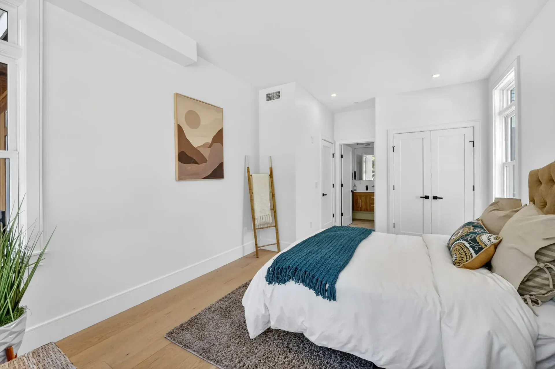 Bright white bedroom with bed, teal throw, abstract wall art, and small rug