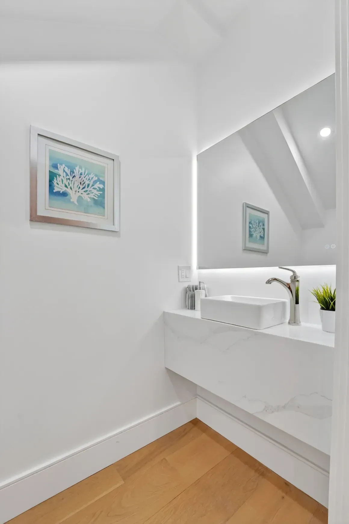 Bright white bedroom with wood floor, large wall mirror, and framed artwork above the bed.