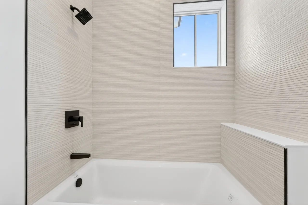 Modern white bathroom with a tub, tiled walls, black fixtures, and a small window