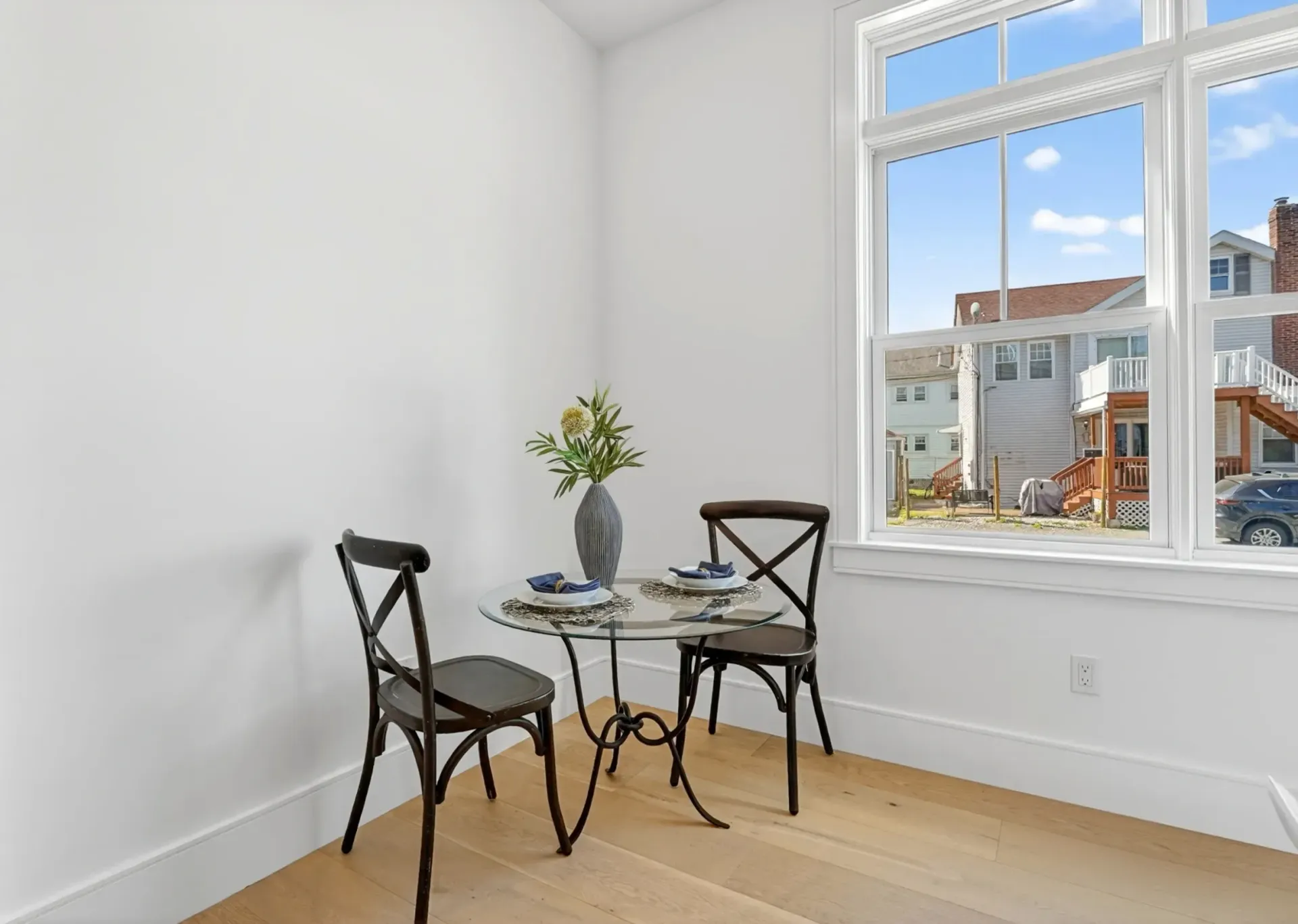 Small dining nook with black chairs and glass table beside a bright window.