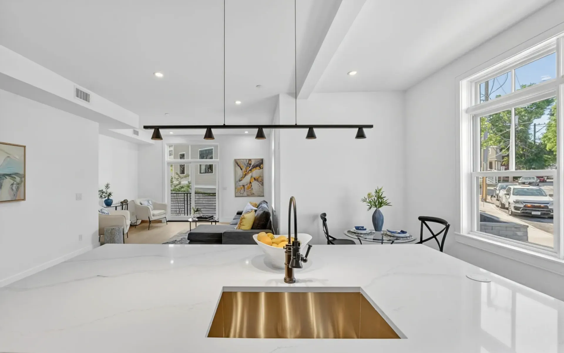Bright modern kitchen with white island, wood sink basin, black pendant lights, and large windows