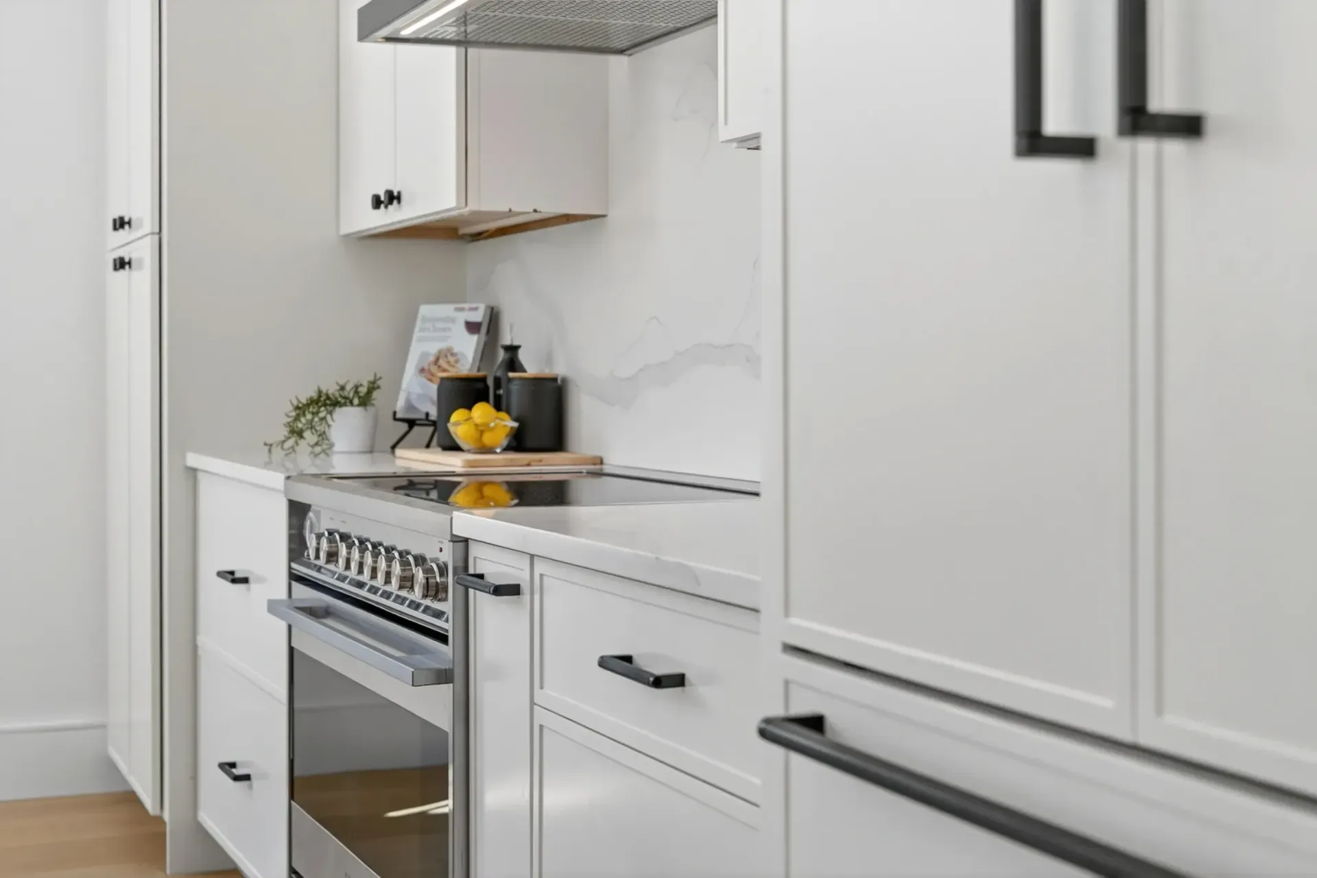 Modern white kitchen with stainless steel oven, marble counters, and black bar stools