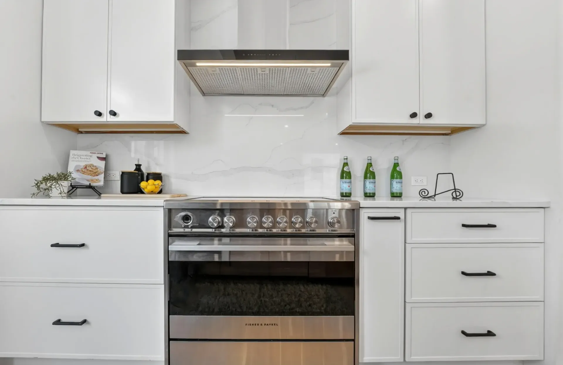 Modern white kitchen with stainless steel oven, marble backsplash, and countertop decor