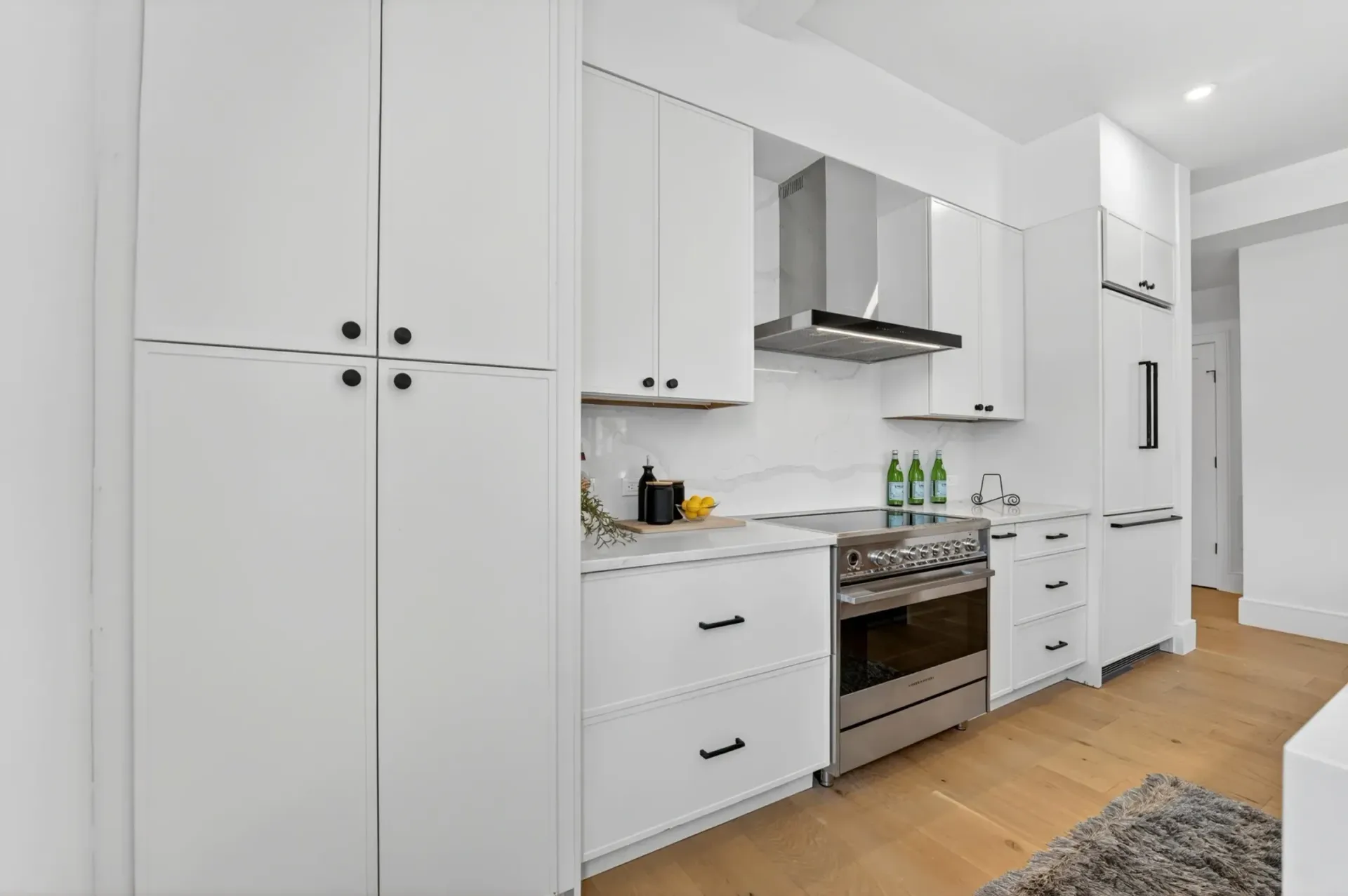Bright white modern kitchen with stainless steel stove, cabinets, and light wood flooring