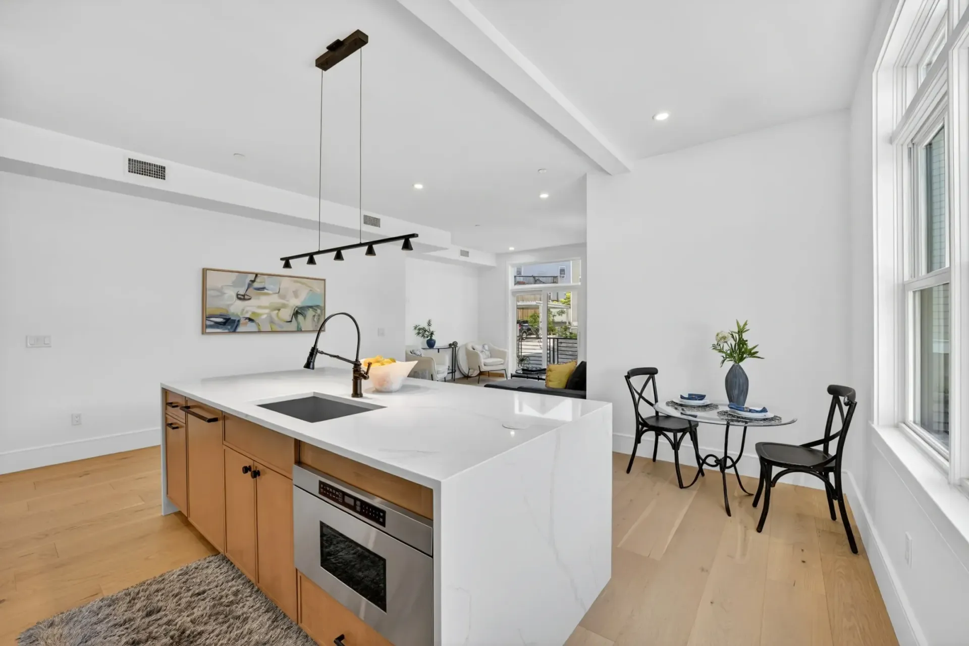 Bright modern kitchen and dining area with white island, wood floors, and large windows