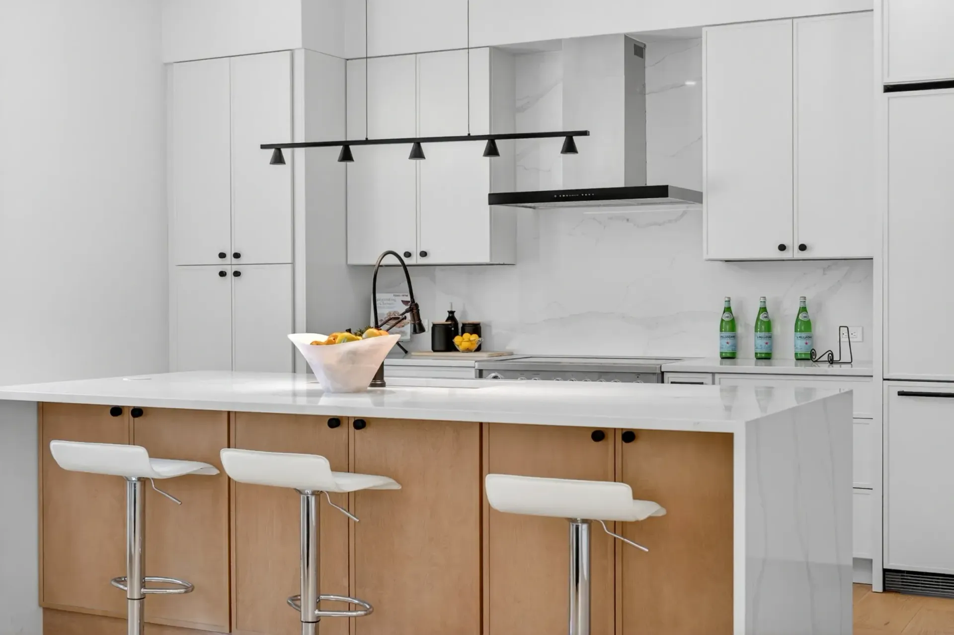 Modern white kitchen with island, bar stools, pendant lights, and fruit bowl