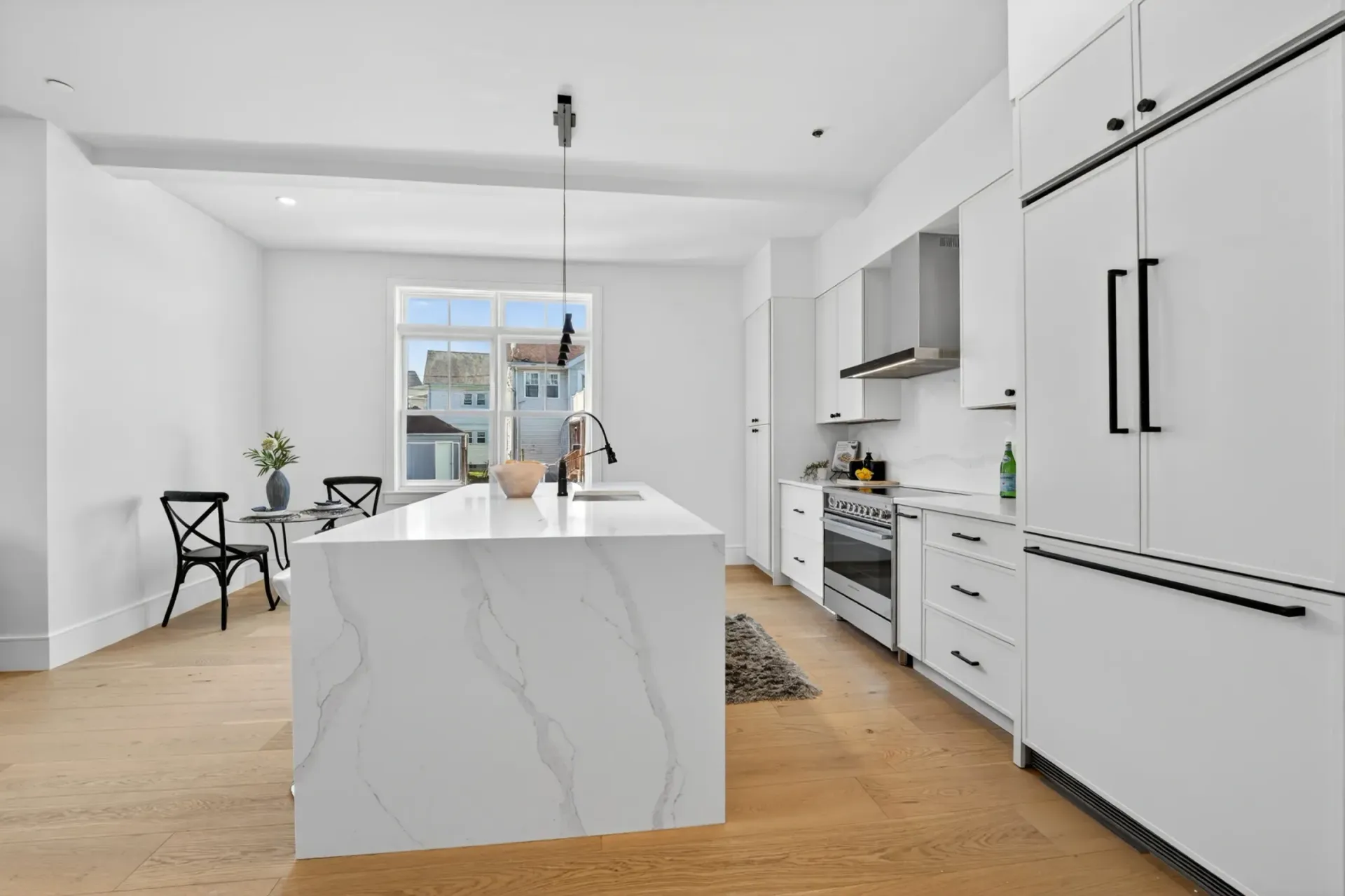 Bright modern kitchen with white cabinets, marble island, and wood floors, open to a dining area.