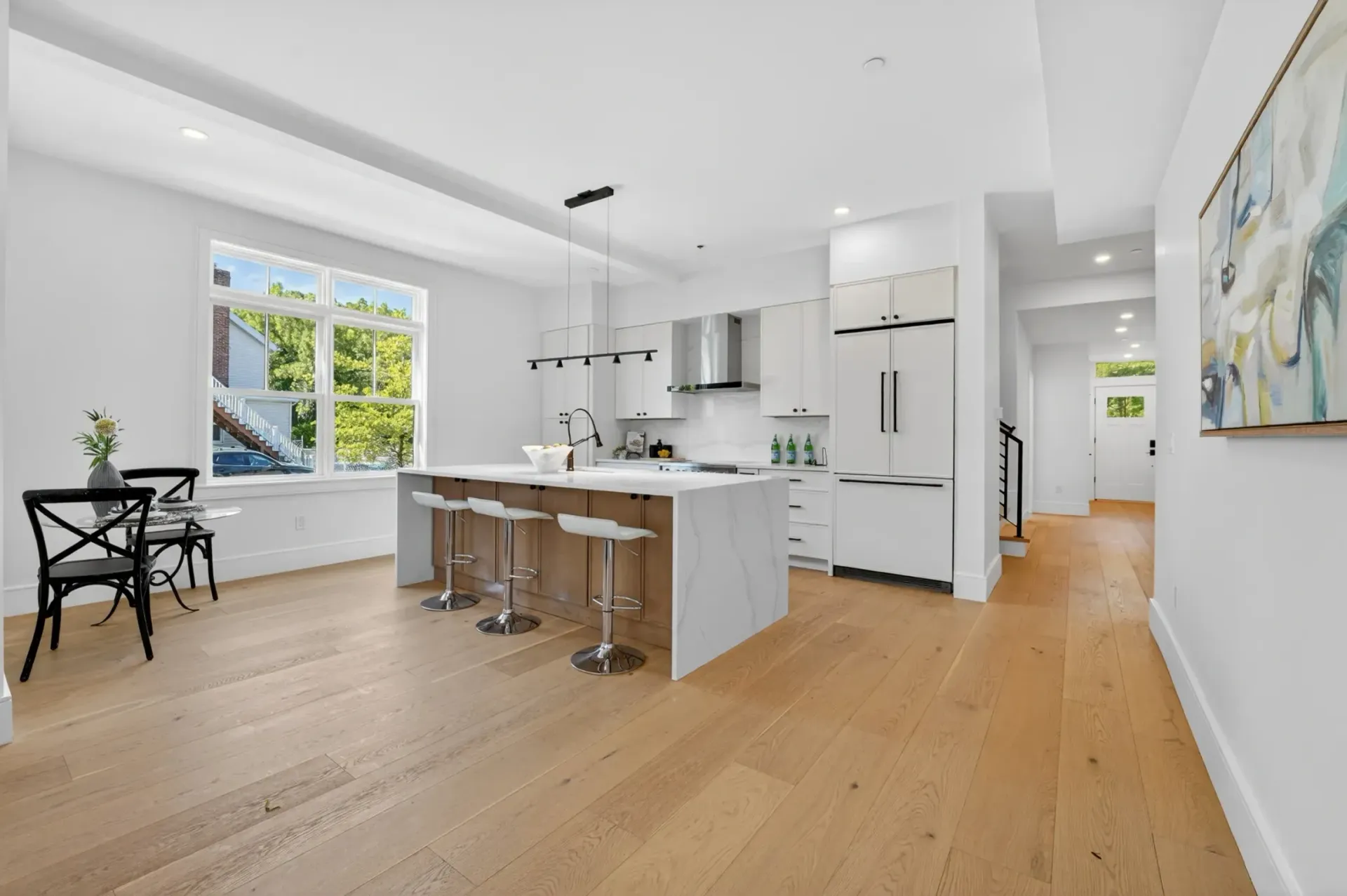 Bright modern kitchen with white cabinets, island stools, wood floors, and a sunlit dining nook