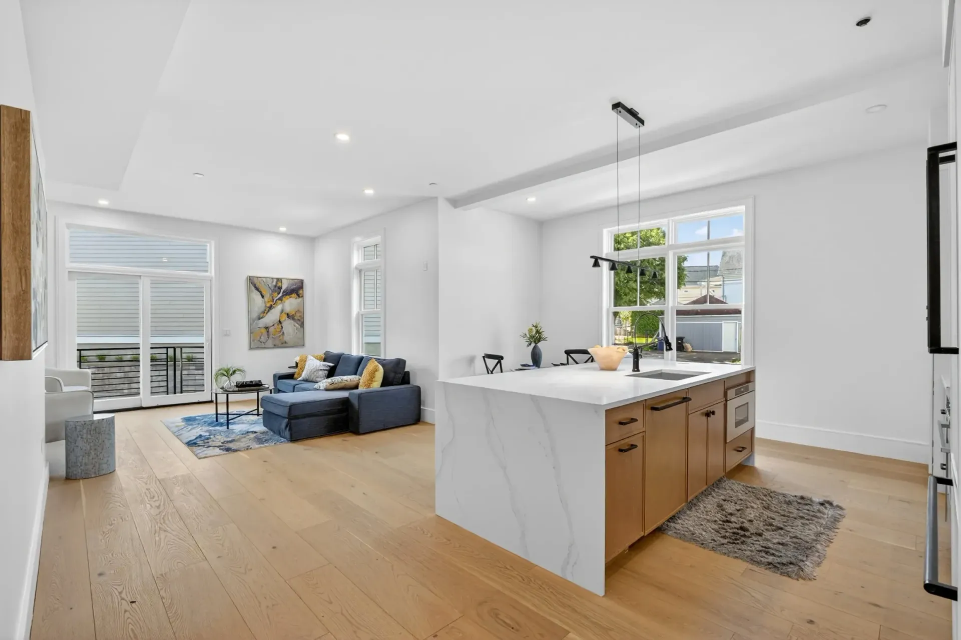 Bright open living room and kitchen with blue sofa, white island, and light wood floors