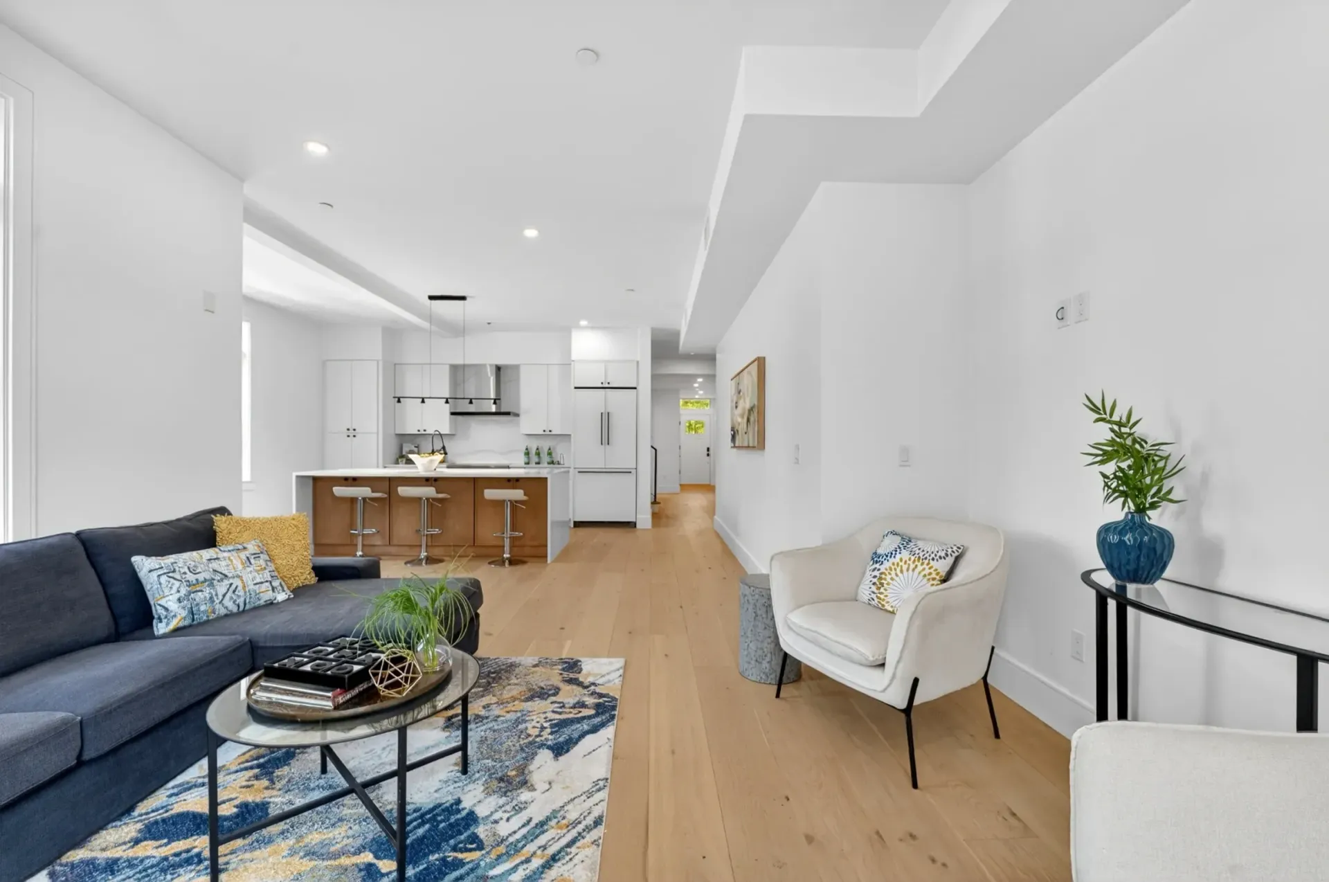Bright open-plan living room with blue sofa, coffee table, armchair, and kitchen island in the background
