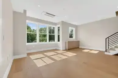 Bright empty living room with large windows, hardwood floors, and a staircase railing
