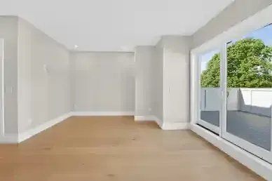 Bright empty living room with light wood floors, white walls, and large sliding glass doors to a balcony