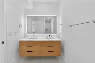 Modern bathroom vanity with double sinks, wood drawers, large backlit mirror, and towel bar on white walls