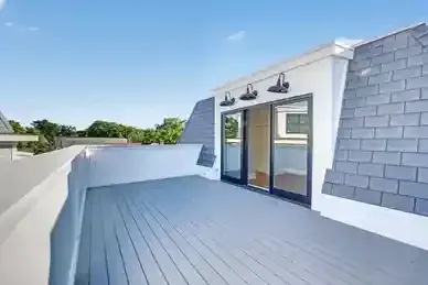 Rooftop terrace with gray decking, white walls, and sliding glass doors under a blue sky