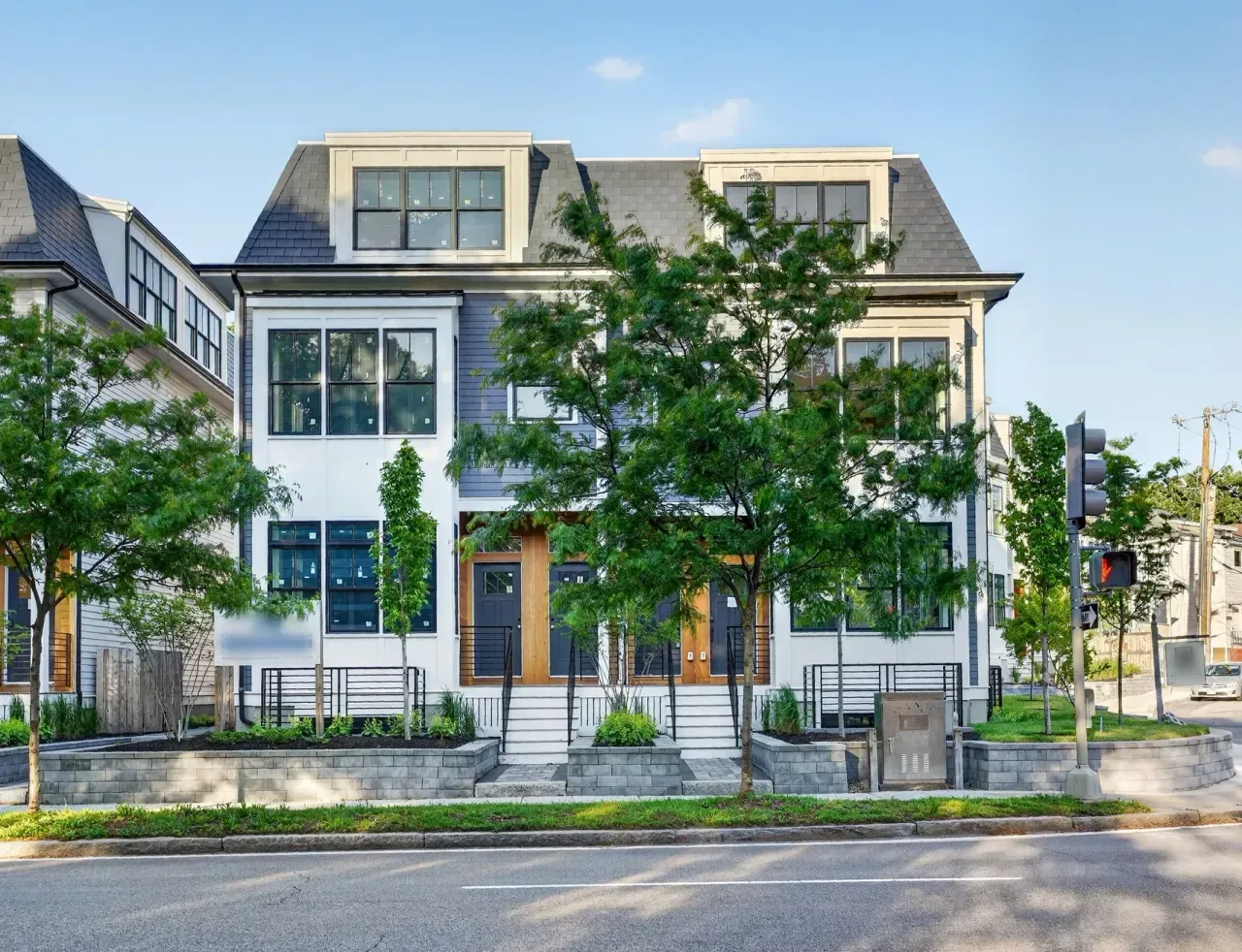 Modern white townhouse with large windows and front trees along a quiet street
