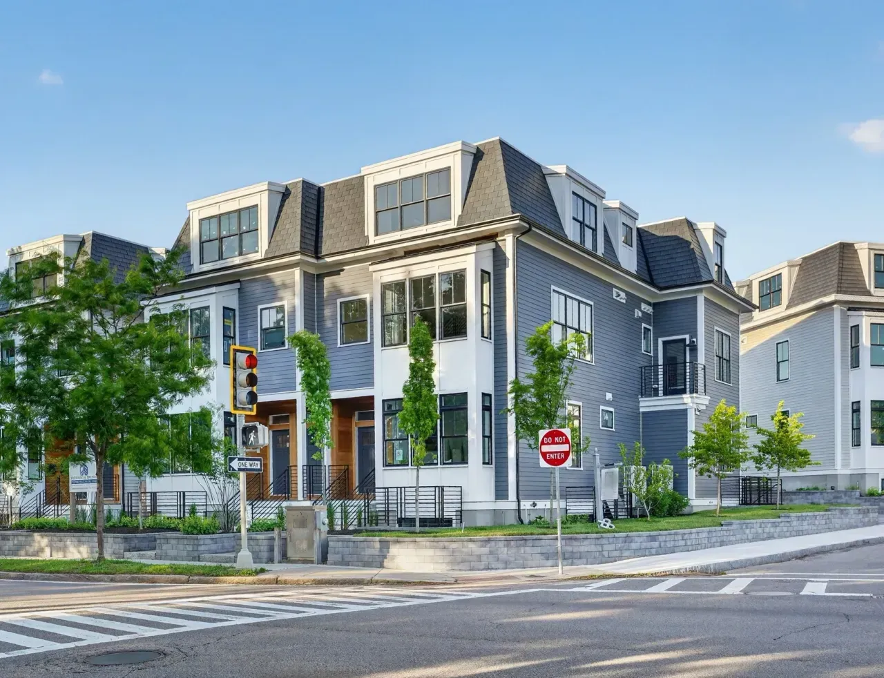 Modern gray townhouse on a quiet street corner with trees, crosswalks, and traffic lights