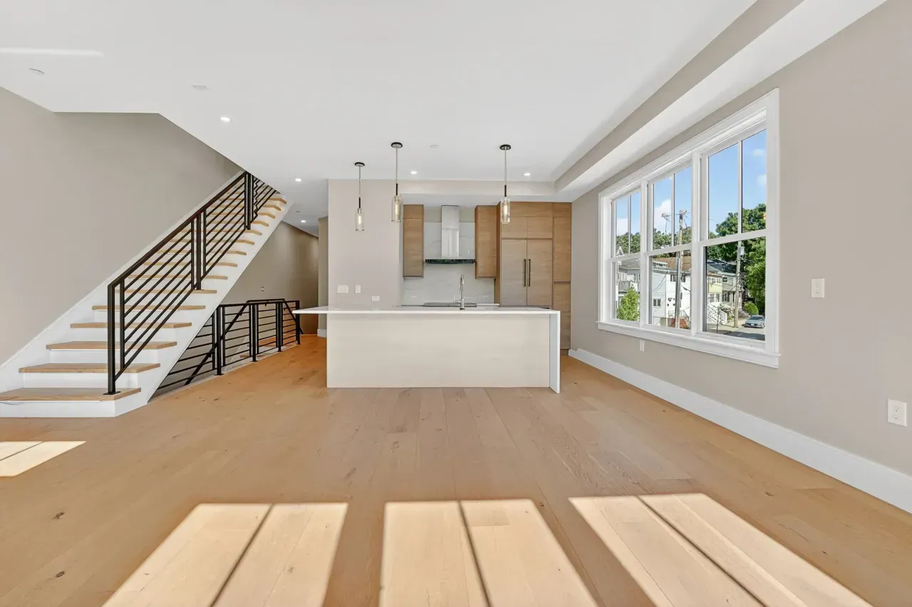 Bright open-concept kitchen and living area with staircase, white island, wood floors, and large windows