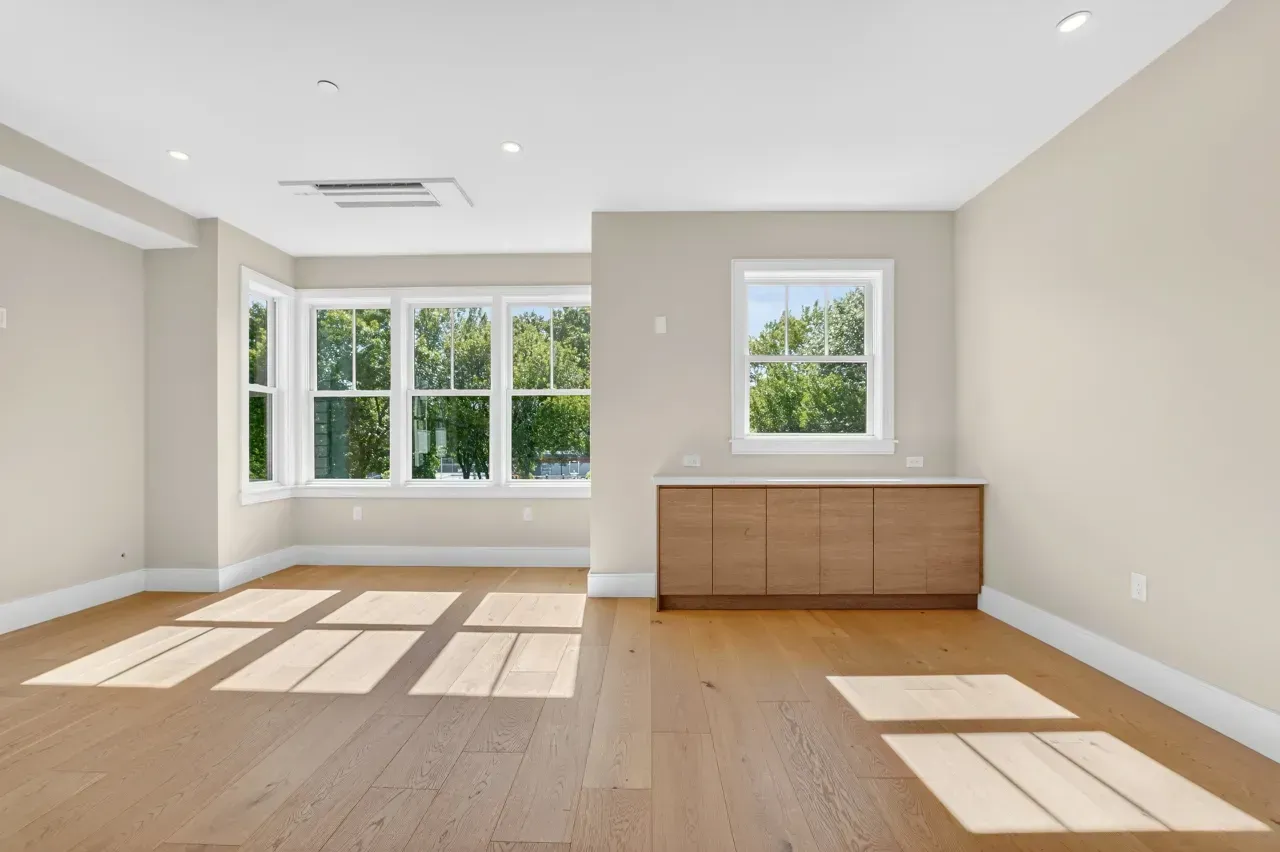 Bright empty living room with wood floors, large windows, and sunlight on the floor